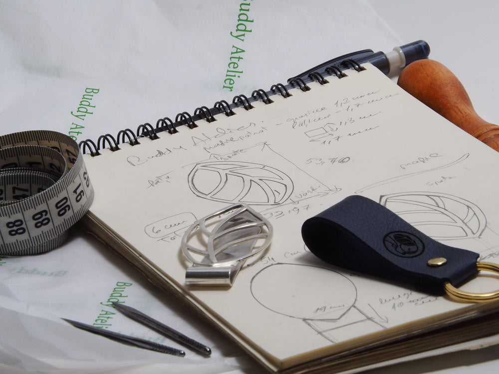 The image shows the design of a key ring made from cactus leather and a money clip made from silver. Also, the image contains the design on paper we made for the silver money clip.